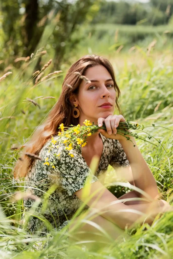 Anna Vlasic sitzt in einer grünen Wiese mit Wildblumen und verkörpert nachhaltiges Leben und bewussten Konsum